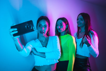 Lifestyle of friends partying in a disco with blue and pink neon lights, taking a selfie with the...