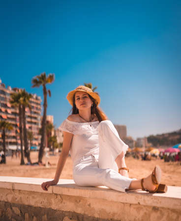 Lifestyle of a young red-haired Caucasian girl dressed in white and with a straw hat on the beaches of Calpe, Valencia. Spain. Enjoying the Mediterranean Seaの写真素材
