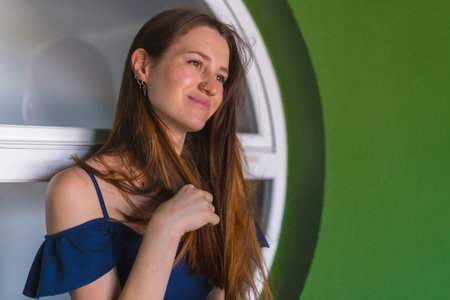 A young pretty redhead Caucasian girl smiling sitting in a blue dress next to a white sale of a...