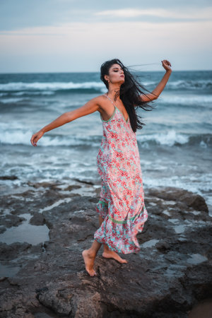 Posing of a brunette Caucasian in a white fabric dress with flowers, on the beach enjoying the holidays by the seaの写真素材
