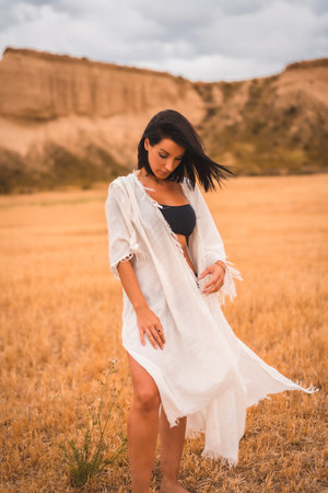 Portrait of a young brunette Caucasian model in a white dress and a black bikini enjoying in the beautiful desert one summer afternoonの写真素材
