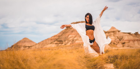 Young brunette Caucasian girl in a white dress and a black bikini enjoying in the beautiful desertの写真素材