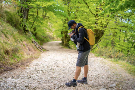 A young father placing the newborn child well in the backpack on a path in the forest heading to the picnic with the familyの写真素材