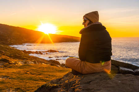 A relaxed young woman watching the sunset in the cove of stones in the Jaizkibel mountain in the town of Pasajes, Gipuzkoa. Basque Countryの写真素材