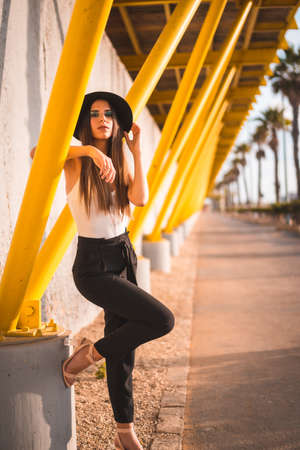 A young brunette in a black hat and pants on a yellow boardwalkの写真素材