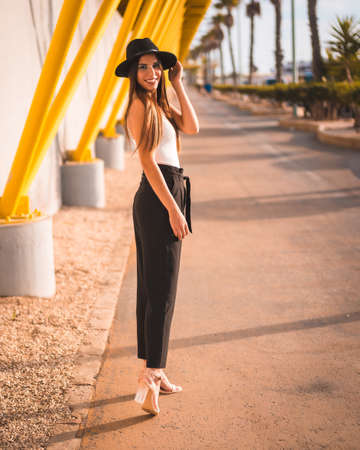 A young brunette in heels, pants and black hat on a yellow boardwalkの写真素材