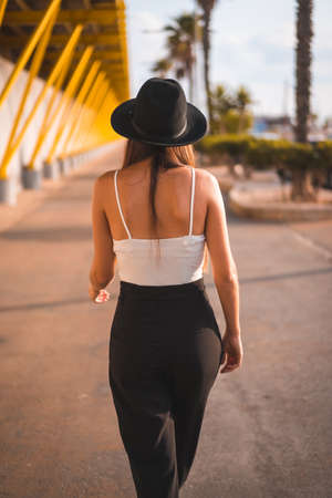 Lifestyle, a young brunette walking through the Mediterranean in heels, pants and black hat on a yellow promenadeの写真素材