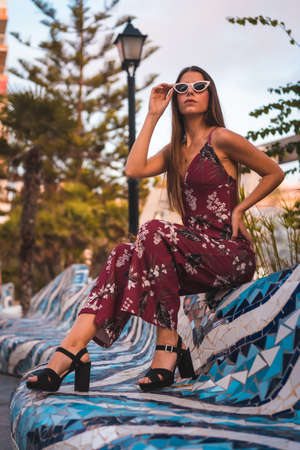 Street Style, a young brunette in a maroon floral dress and modern white sunglasses enjoying the summer at the golden hour in the cityの写真素材