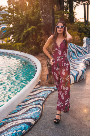 Street Style, a young brunette in a maroon floral dress and modern white sunglasses enjoying the...