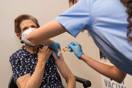 San SebastiÃ¡n, Gipuzkoa. Spain. May 8, 2021: A scared elderly woman receiving the dose prick by a young nurse at the vaccination center, covid-19. Coronavirusのeditorial素材