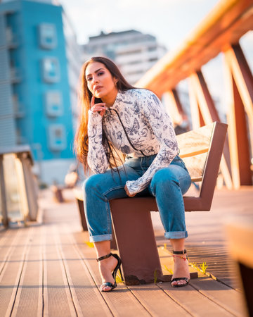 A Latin girl in jeans and a white t-shirt in the city at sunset. On a bridge looking at the city...