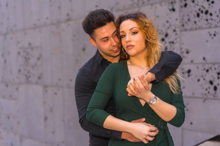 Fashionable pose of a Caucasian loving couple in a blue suit and green dress, hugging in the city