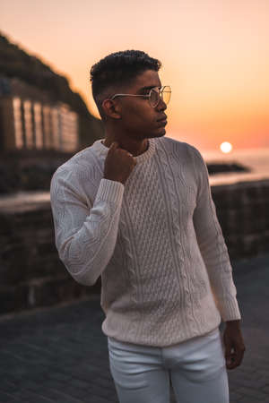 Summer lifestyle, a young Latino enjoying summer vacations. dressed in white with pants and sweater, walking by the seaの写真素材
