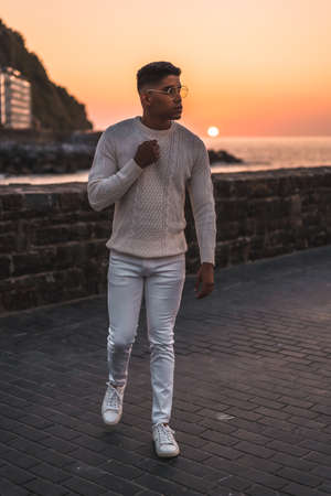 Summer lifestyle, a young Latino enjoying summer vacations. dressed in white with pants and sweater, walking by the seaの写真素材