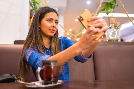 Street Style in the city, a brunette Caucasian girl in a denim shirt having tea in a coffee shop....