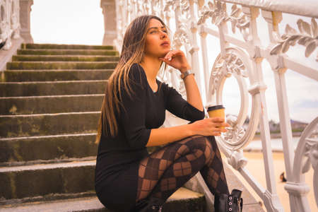 Lifestyle in the city, Caucasian brunette in a short black dress and with plaid tights sitting enjoying the vacation in summerの写真素材