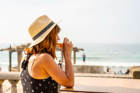 Summer vacation lifestyle. Young caucasian girl in a hat having a soda next to the beachの写真素材