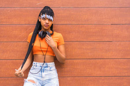 Lifestyle with a young trap dancer in the city. Black grind girl of African ethnic group with orange t-shirt and cowboy pants, with headphones on a wooden backgroundの写真素材