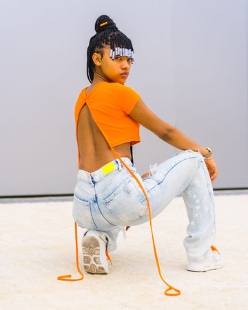 A young trap dancer with braids. Black ethnic girl with orange t-shirt and cowboy pants. Backs of...