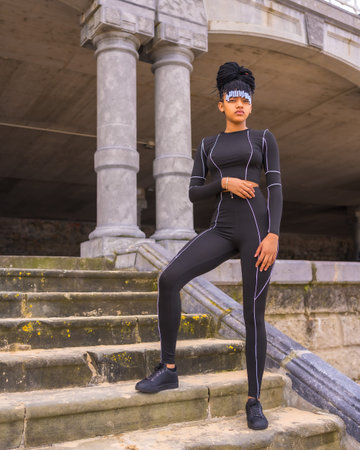 Black ethnic girl with braids with with black full body suit. I posed on some stairs next to the...