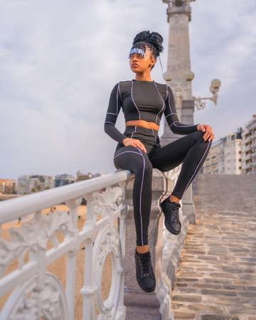 Beautiful Dominican Ethnic Girl with with braids with full body suit. Fashion, sitting on the beach railing in summer with sweet and seductive lookの写真素材