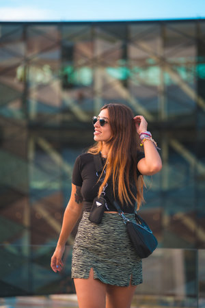 Beautiful young caucasian brunette businesswoman outside the green glass office building background. Portrait of the girl with sunglassesの写真素材