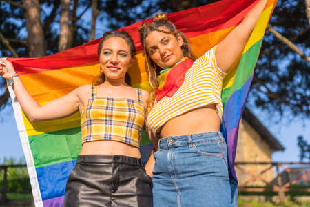 A closeup shot of two young Caucasian females holding LGBT pride flag outdoorsの写真素材