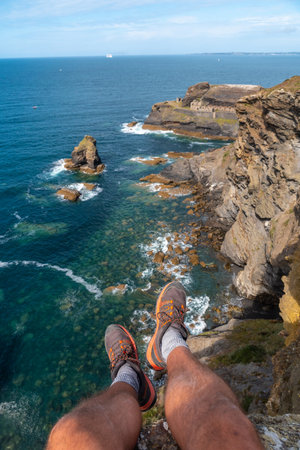 A young man sitting on the shoreline looking at the Fort des Capucins a rocky, clifftop islet in the town of Roscanvel on the Crozon Peninsula in France.の写真素材