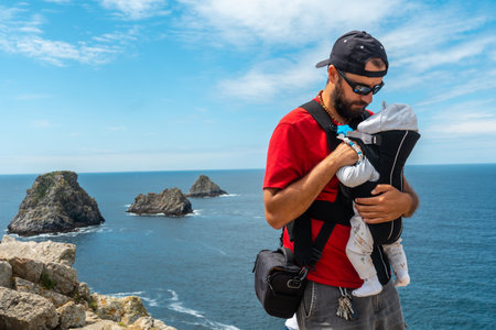 A young man with backpack and baby looking at the sea at Pen Hir Point on the Crozon Peninsula in...
