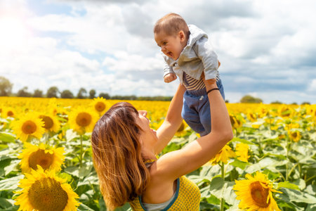 Portrait of Caucasian mother and her baby laughing in a sunflower setting, summer lifestyleの写真素材
