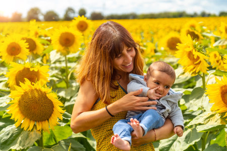 Portrait of Caucasian mother and her baby laughing in a sunflower setting, summer lifestyleの写真素材