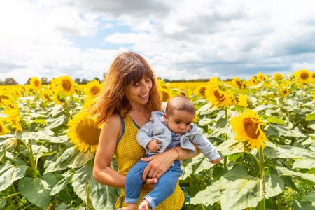 Portrait of a Caucasian mother and her baby having fun in a field of sunflowers, summer lifestyleの写真素材