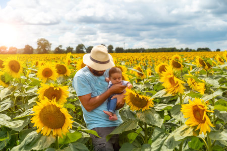 Portrait of a Caucasian father and his baby having fun in a field of sunflowers, summer lifestyleの写真素材