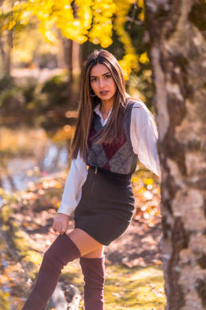 Autumn lifestyle, a young Caucasian brunette, in a park next to a tree with a smiling lookの写真素材