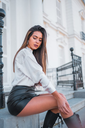 Lifestyle, fashionable pose of a young brunette in a black leather skirt and shirt sitting on some stairs one autumn afternoonの写真素材