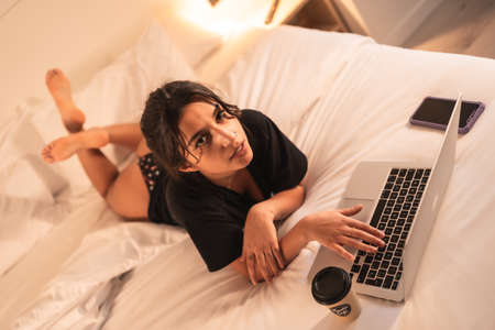 Relaxed sexy brunette girl on the bed with a computer and coffeeの写真素材
