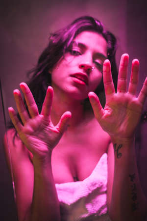 Lifestyle, sexy brunette Caucasian girl with towel at the end of the shower with sensual gaze, with pink led light, posed inside the wet showerの写真素材