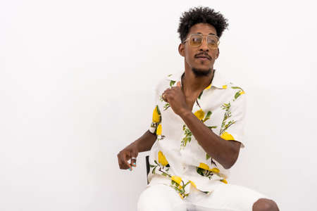A young Cuban man with curly hair sitting in a white flowered shirt and glasses. Smiling and dancing on a white backgroundの写真素材
