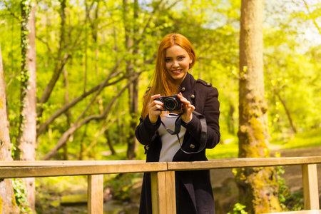 Woman photographer with a black jacket enjoying in an autumn park, smiling and enjoying taking...