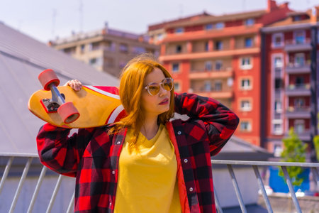 Skateboarder woman with a yellow shirt, red plaid shirt and sunglasses, in a pose with skateboardingの写真素材