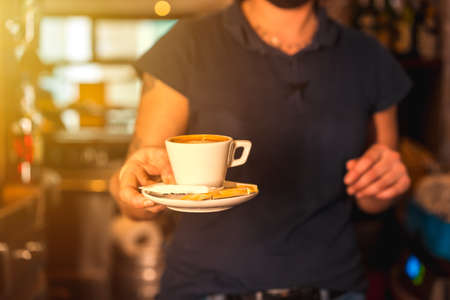 A waitress with a white cup of decaf coffee handing it to a customerの写真素材