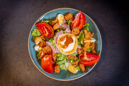 Salad with ham, cheese and chicken on a black background, on a green plateの写真素材
