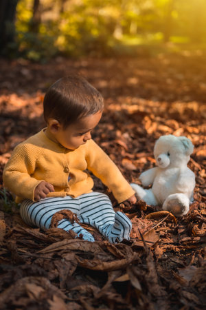 Six-month-old baby sitting in the leaves of the trees with a white bear in the park on an autumn sunset. Natural lightingの写真素材