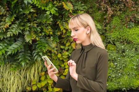 Caucasian blonde entrepreneur girl in a business park in a corner of nature, reviewing emails with...