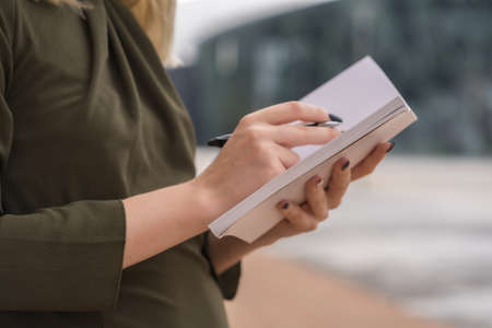 Unrecognizable person in a business park pointing notes in the agenda, young blonde in a green shirt leaning against a wooden wall, copy space and pasteの写真素材