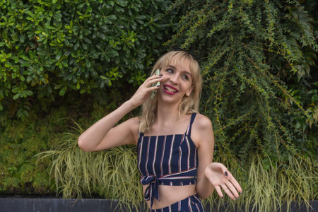 Entrepreneur girl in a business park on a green wall of plants, young blonde smiling making a call...