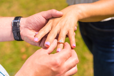 Hands of two unknown persons in a marriage request, detail a man putting the marriage engagement...