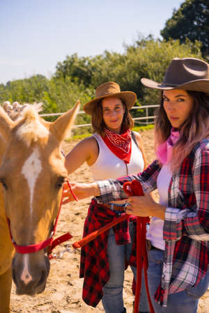 Two cowgirl women caressing a horse on a horse riding, with South American outfits, the two young women posingの写真素材