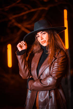 Girl in a hat in a portrait at night on a parcel. Caucasian brunette model looking at camera, lifestyle and streetの写真素材