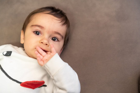 Baby suffering the pain of his first teeth, lying on the sofa at home with a white sweater